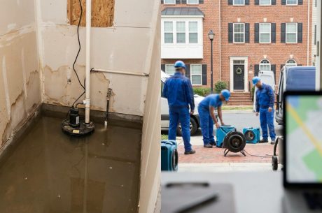 Water damage restoration crew arriving at an Alexandria, VA home with drying equipment while standing water and a sump pump are visible inside the property.