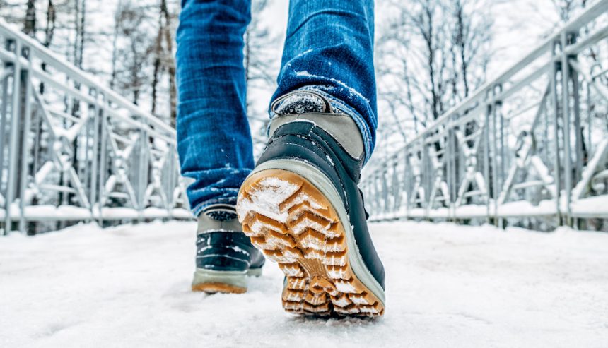Man's legs in black with orange boots walking in the snow