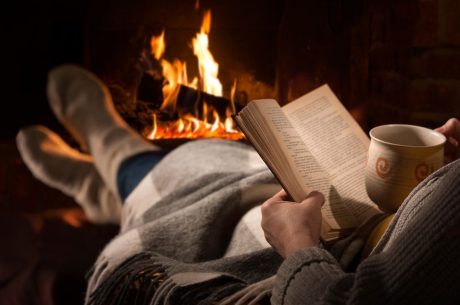 A woman reading a book by a fire. Winter fire safety tips.