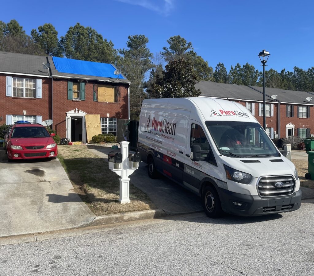 The fire-damaged building has a tarp over the roof and boards over the windows.