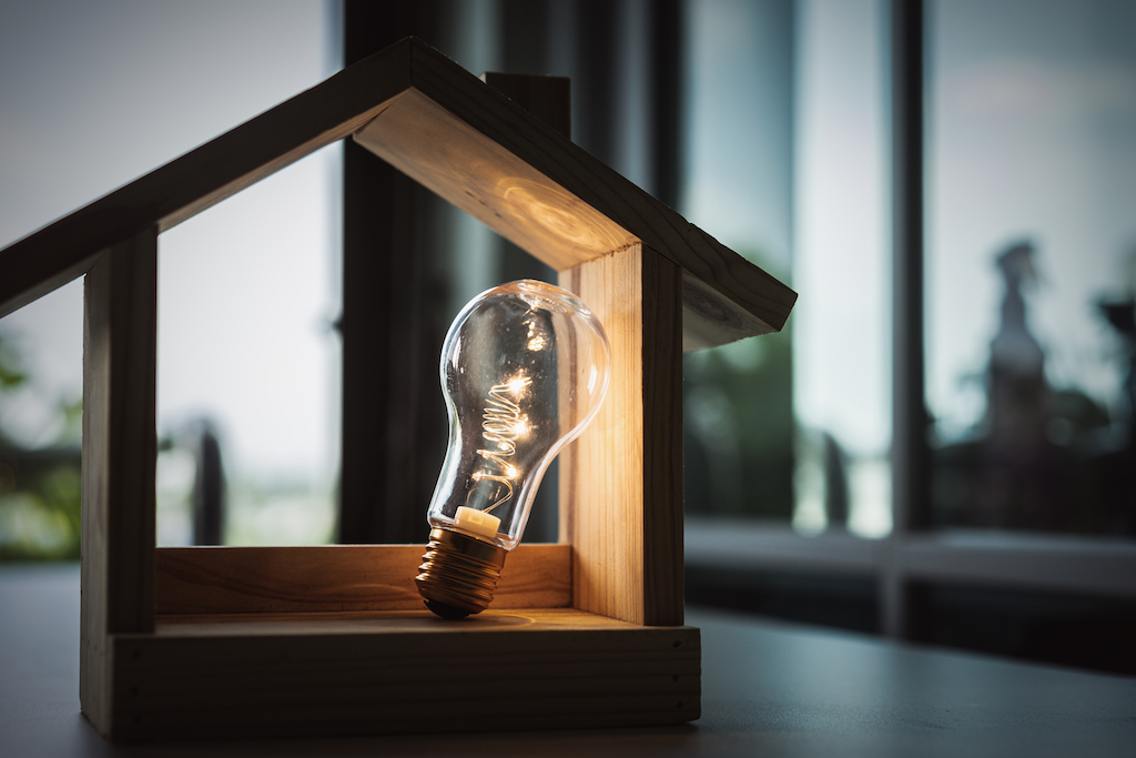 A light bulb inside a wooden house-shaped display, symbolizing electrical tips for home improvement.