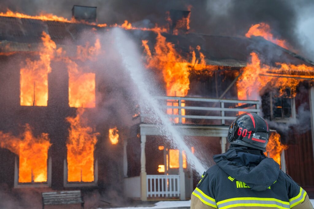 A firefighter sprays water on a burning building engulfed in flames during a fire emergency.