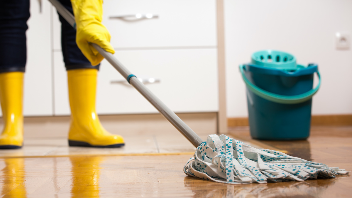 Maid in gumboots mopping tiled floor in kitchen. Housekeeping and home hygiene concept