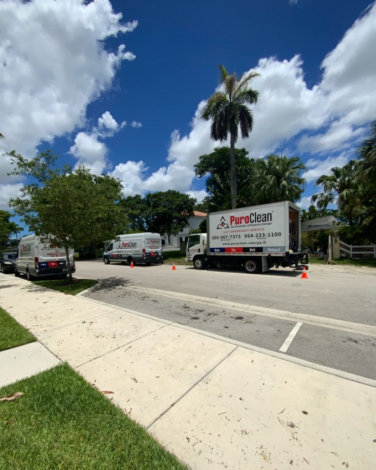 Two water damage restoration trucks parked on a residential street under a bright blue sky with scattered clouds.