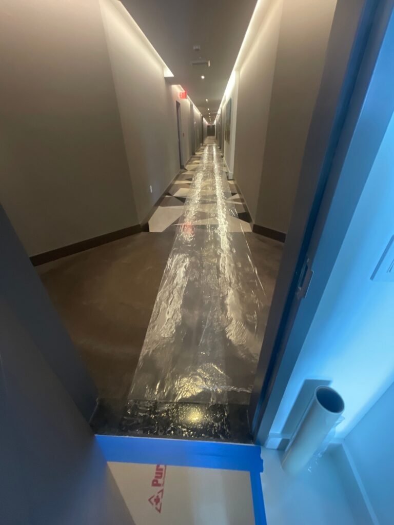 A long hallway in a condo with plastic sheeting on the floor, indicating mold remediation efforts.