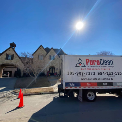 A PuroClean emergency service truck is parked on a street in front of a large stone house on