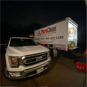 A white PuroClean Ford truck and open service trailer are ready for emergency work at night.