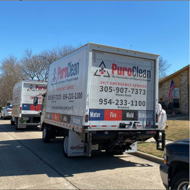 Two PuroClean emergency service trucks, with a worker in a hazmat suit, parked