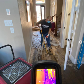 A PureClean technician removes water-damaged wood flooring as an infrared camera scans for moisture.
