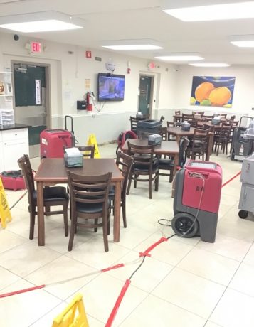 Water damage restoration in a commercial dining room with drying machines and wet floor signs.