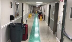 Long hallway with a green floor runner, cleaning equipment, and multiple wet floor signs.