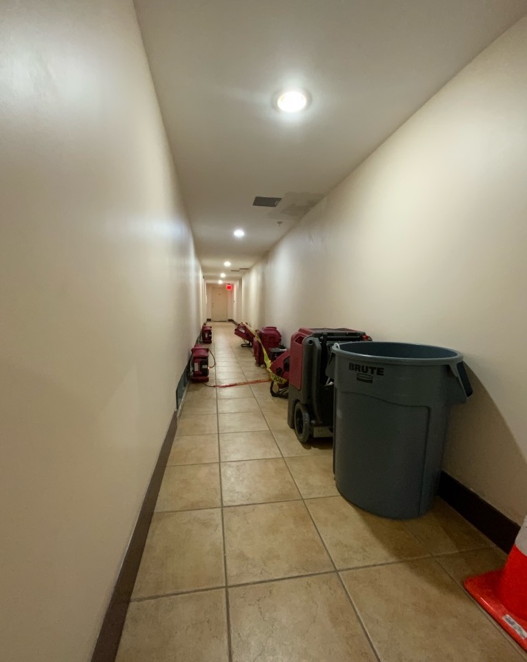 Water damage restoration equipment, including red air movers and a large grey trash can, lines a long