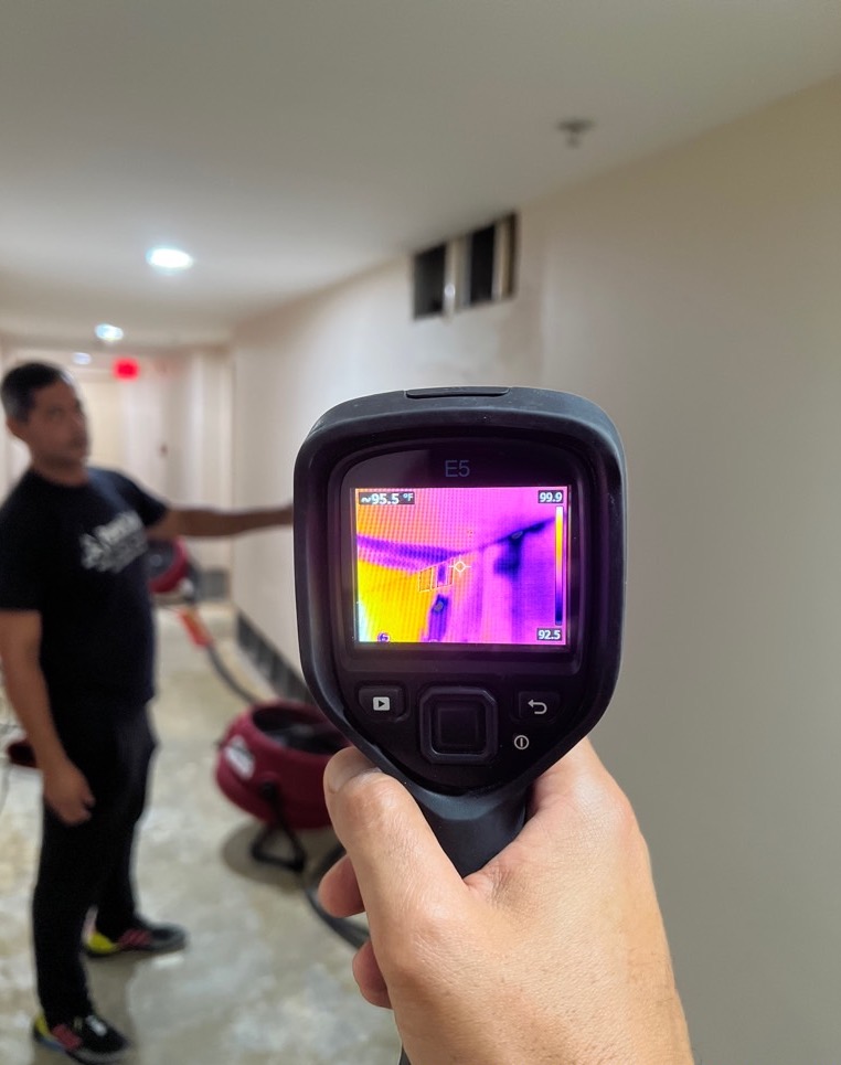 Technician uses a thermal camera to detect temperature anomalies on a building wall. TITLE: