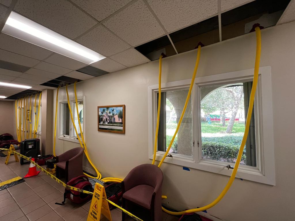Commercial building undergoing water damage restoration with yellow hoses and drying equipment.