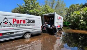PuroClean emergency service vehicles are working in murky floodwaters under a clear sky.