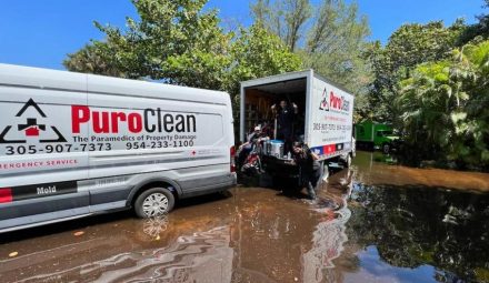 PuroClean emergency service vehicles are working in murky floodwaters under a clear sky.