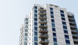 A modern high-rise building with many windows and balconies stands tall against a clear sky.