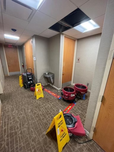Water damage restoration in a commercial hallway with equipment and caution signs.