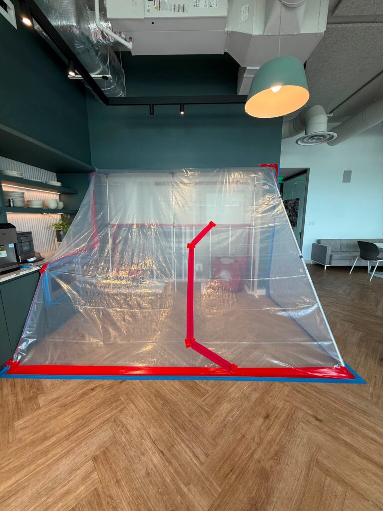 A plastic dust containment tent is set up in a contemporary office kitchen area.