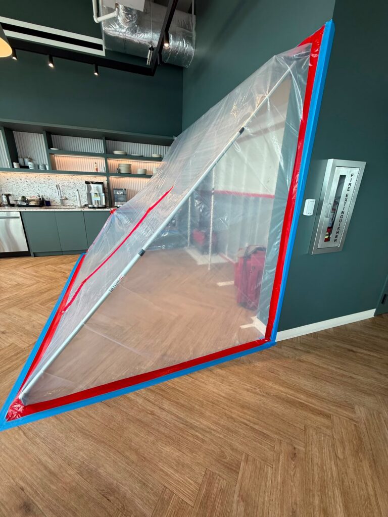 A temporary clear plastic dust barrier, taped with red and blue, separates a modern