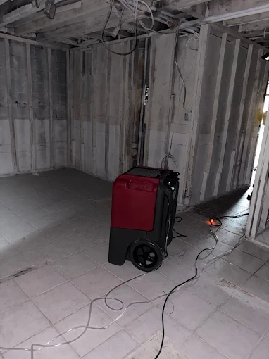 A red dehumidifier sits in a partially renovated room with exposed walls and electrical wires after water damage.