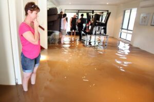 A woman stands in a flooded house with muddy water covering the floor, as others