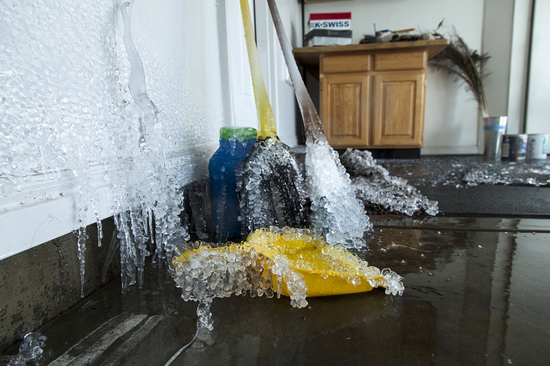 Icicles cover a wall and cleaning tools, with standing water on the floor from severe indoor freezing