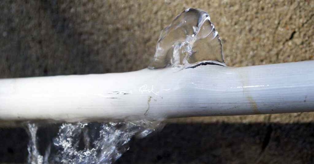 Water leaks from a white pipe, spraying upwards and dripping downwards.