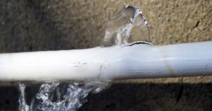 Water leaks from a white pipe, spraying upwards and dripping downwards.