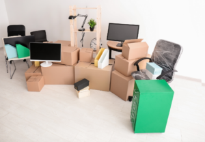 A room filled with cardboard moving boxes, office furniture, and monitors, ready for an office