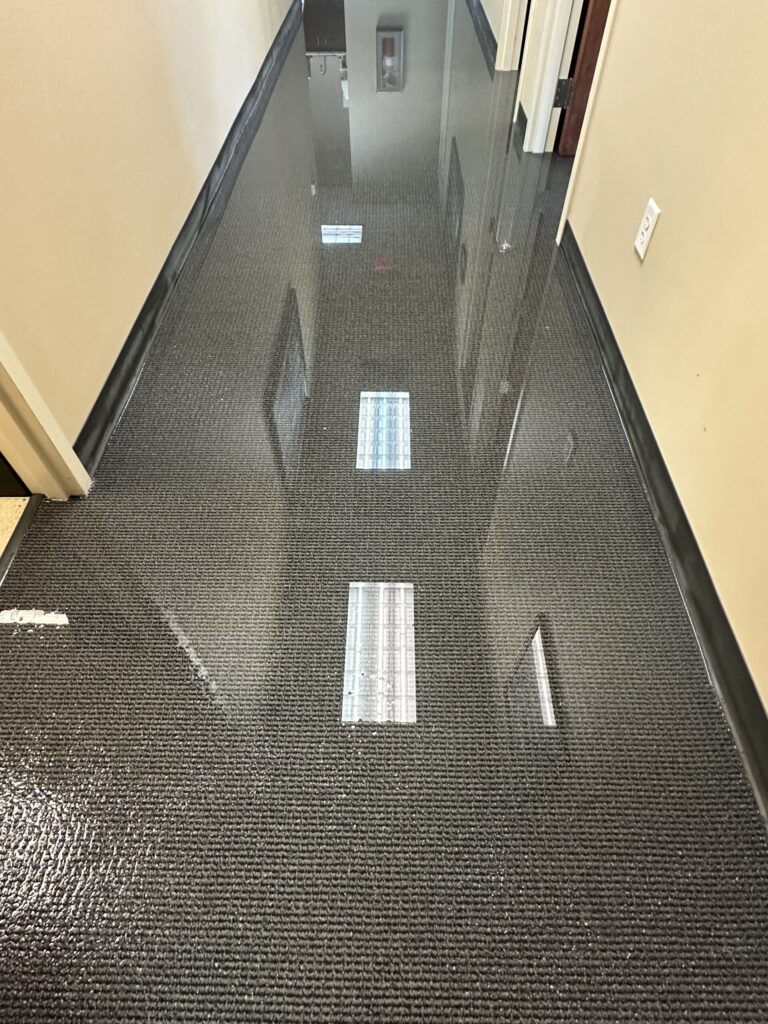 A long hallway with a dark textured floor is completely covered in reflective standing water.