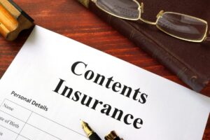 A contents insurance document with personal details, a fountain pen, reading glasses, and a book on a wooden desk.