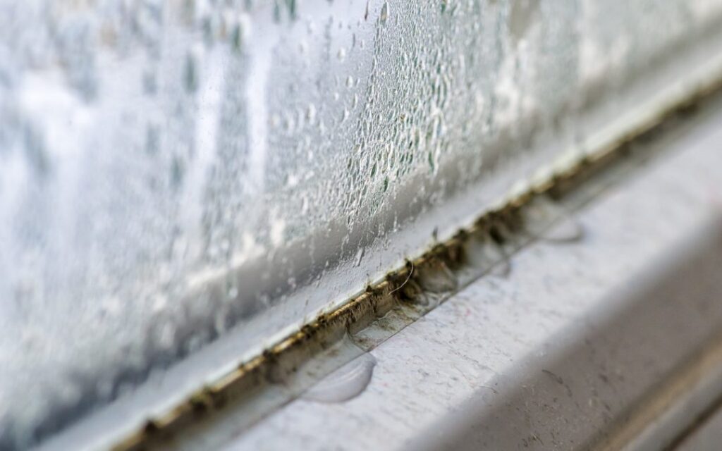 Heavy condensation covers a dirty window pane with visible grime and water droplets on the frame