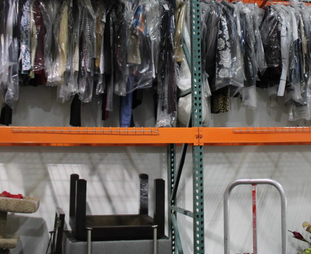 Rows of dry-cleaned garments in plastic bags hang on a metal storage rack. TITLE: