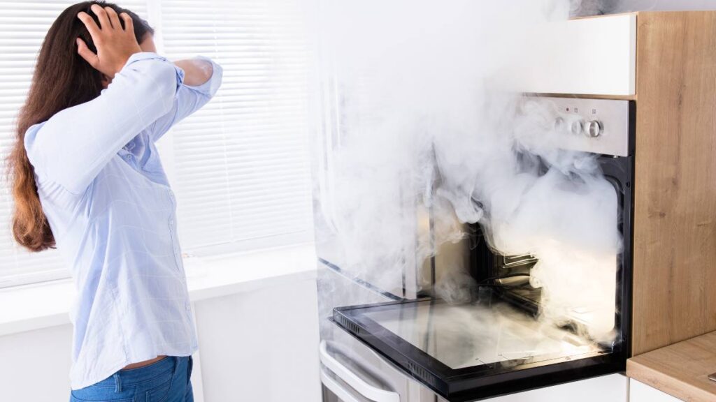 Thick smoke billows from an oven while a person holds their head in distress. TITLE: