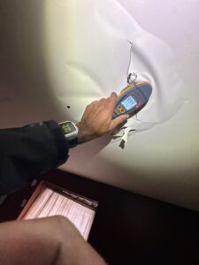 A hand holds a moisture meter displaying "999" against a severely water-damaged, sagging white ceiling.