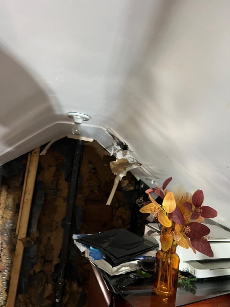 Damaged white attic ceiling with a bare light bulb, exposed insulation, and a