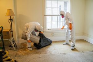 Professionals in hazmat suits perform remediation work in a room with removed carpet. TITLE