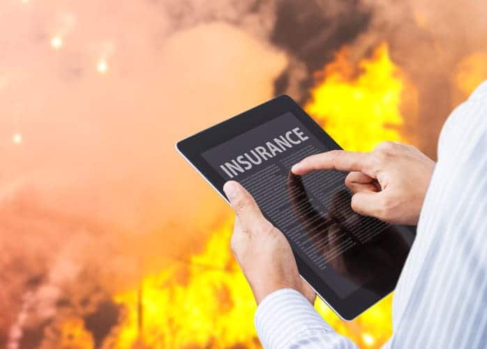 Hands tap a tablet screen showing 'INSURANCE' while a fire rages in the background