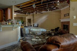 A destroyed home interior features a collapsed ceiling exposing beams, debris-covered floors, and