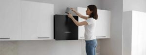 A woman installs a gray filter into a black wall-mounted kitchen air purifier. TITLE