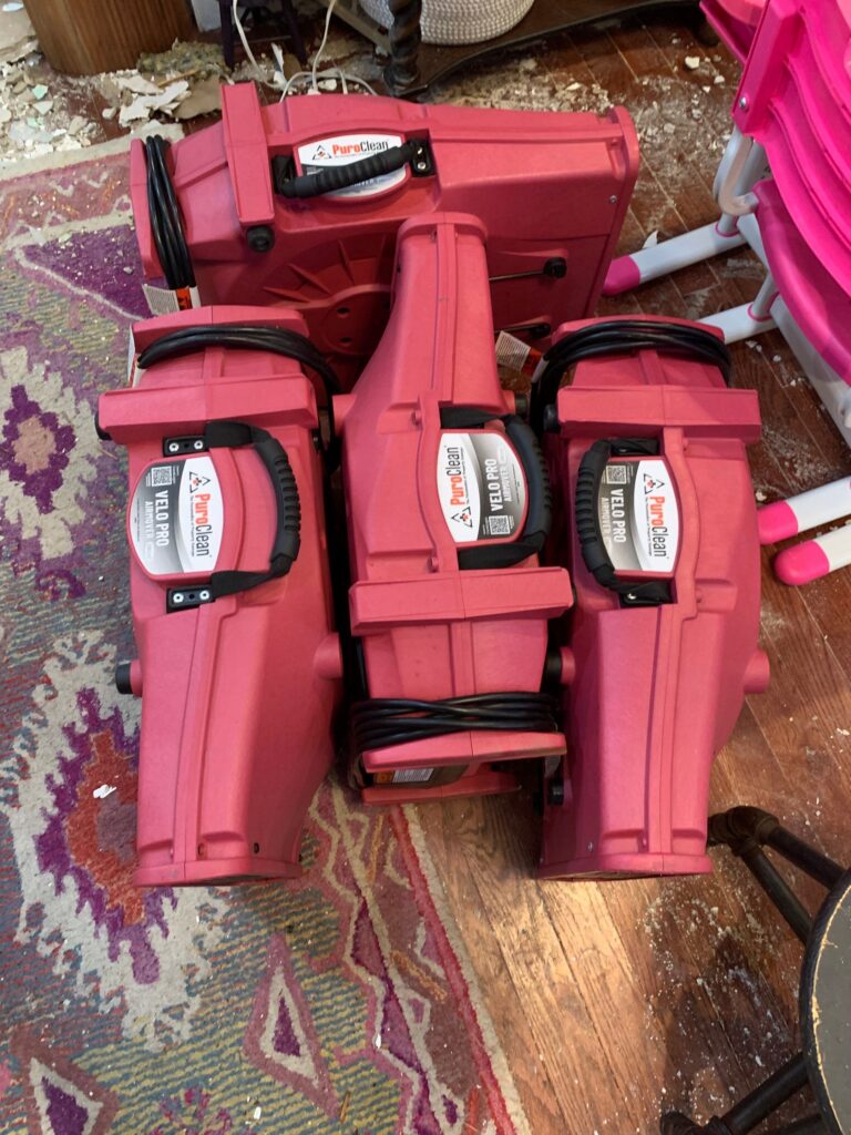 Three red PuroClean Velo Pro airmovers are positioned on a debris-covered floor
