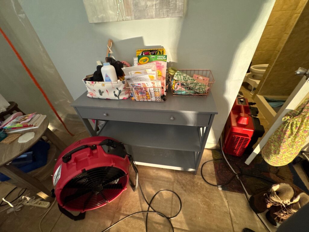 Two red industrial fans dry a tiled room with a gray console table and various household