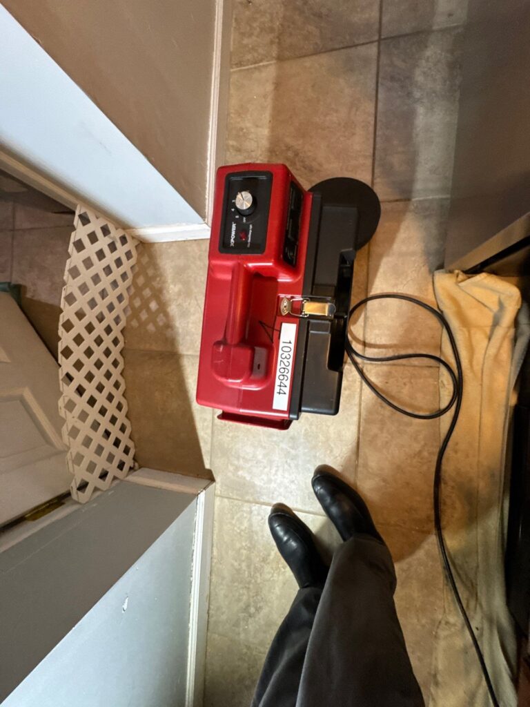 A red and black XPOWER air mover sits on a tiled floor next to a person's