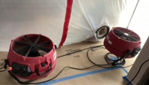 Two red industrial air movers sit on a protective floor covering next to a white plastic