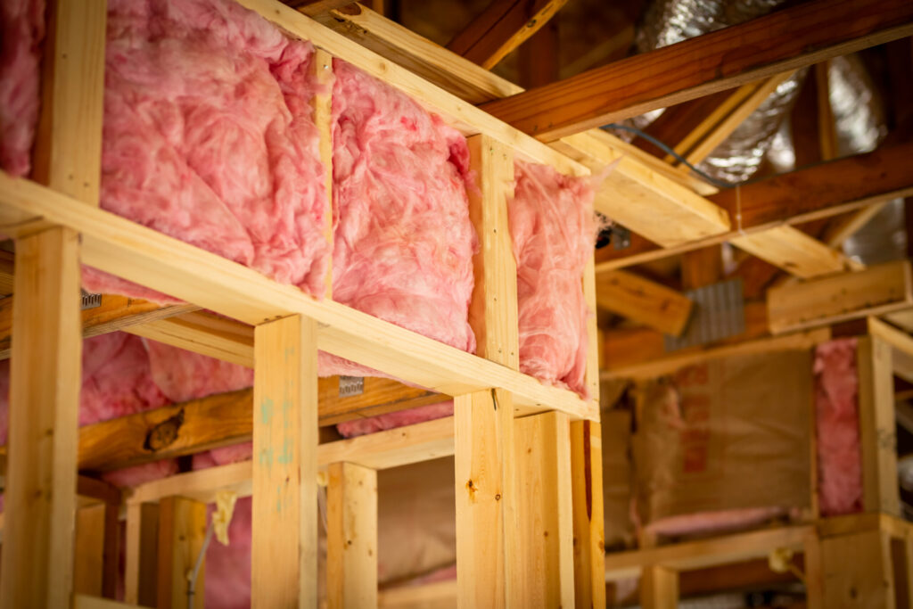 Pink fiberglass insulation fills the wooden framework of a building under construction.