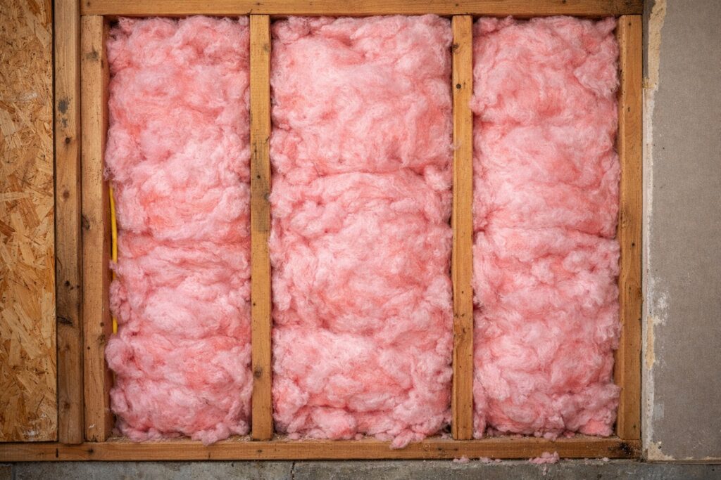Pink fiberglass insulation fills the spaces between wooden studs in a wall under construction. TITLE
