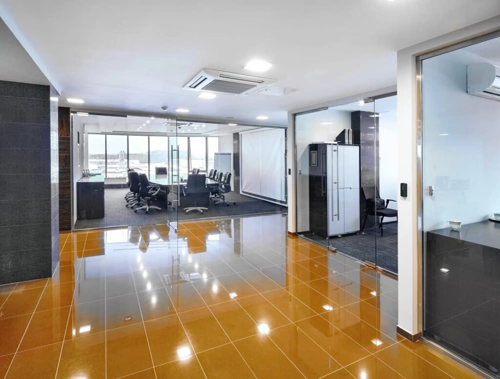 Spacious modern office with reflective orange floor and glass-enclosed meeting rooms. TITLE: