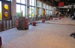 A spacious interior undergoing renovation, featuring exposed walls, concrete floor, and multiple red drying fans.