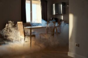 Thick smoke billows around a wooden dining table and chairs in a sunlit room
